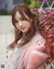 A woman in a pink sweater leaning against a wall.