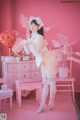 A woman in a white lingerie posing in front of a pink wall.